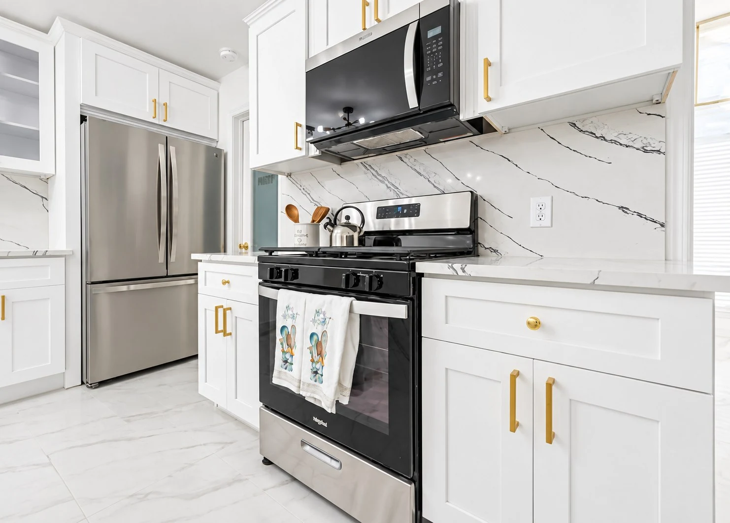White shaker cabinets and gold hardware around a stainless steel range and refrigerator
