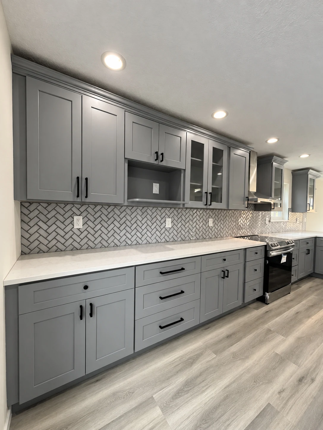 Gray shaker cabinets with dark hardware, glass-front uppers and a patterned backsplash