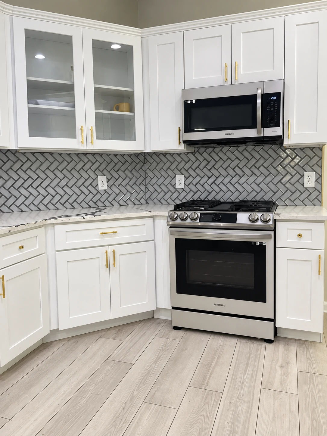 White cabinets with glass-front doors, gold pulls and a gray patterned backsplash