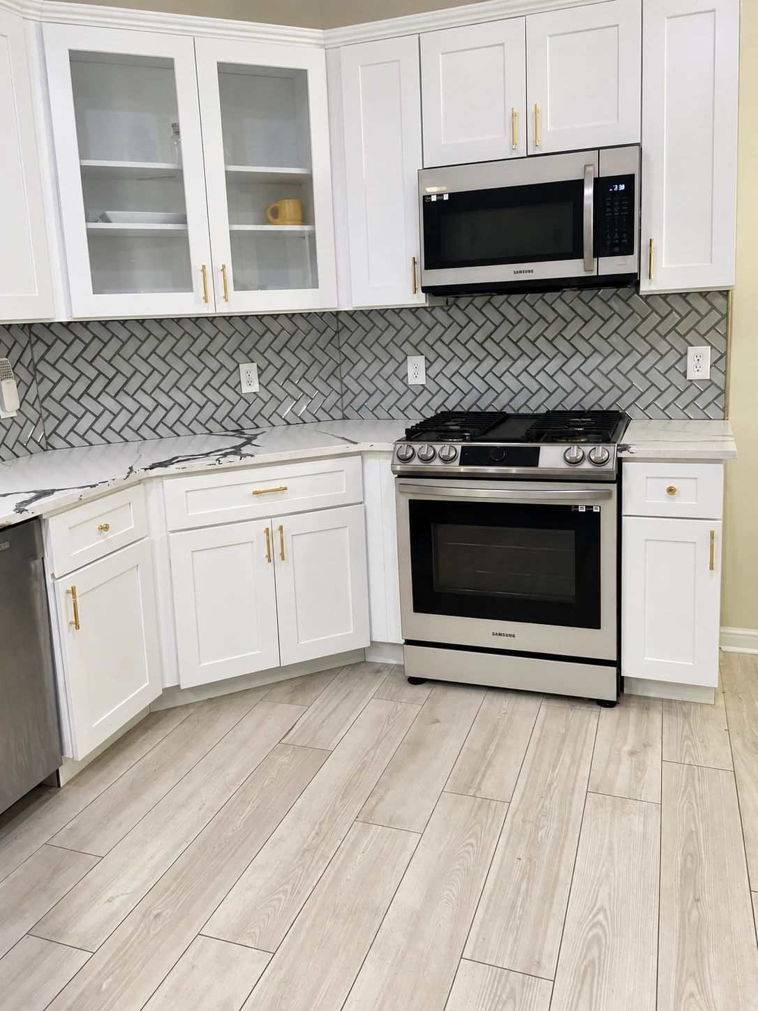 White cabinets with glass-front doors, gold pulls and a gray patterned backsplash — another view